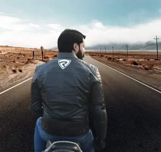 A man wearing casual leather jacket riding a motorcycle on a road